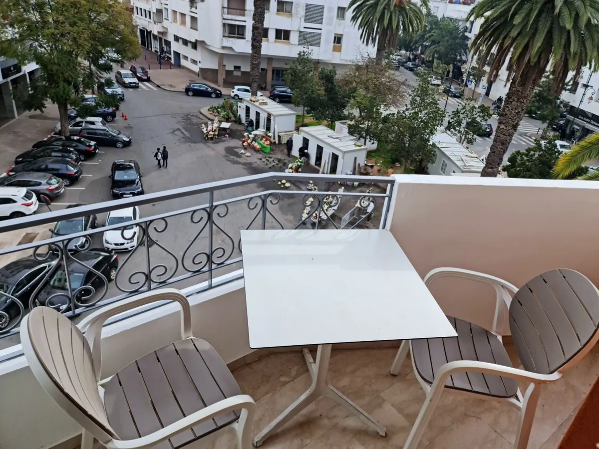 Vue plongeante du balcon sur la place, les voitures garées et les palmiers