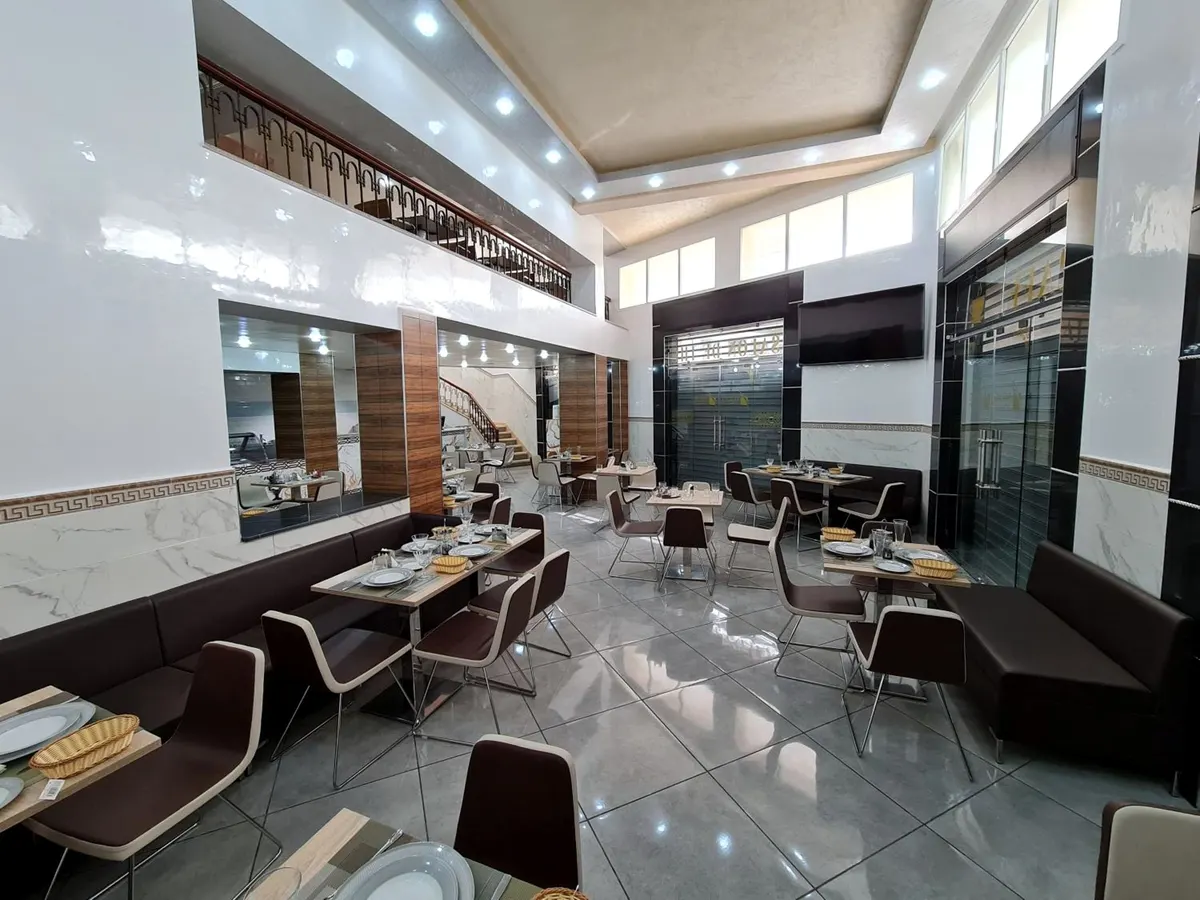 Salle du café sur double hauteur avec mezzanine, sol carrelé clair, tables dressées