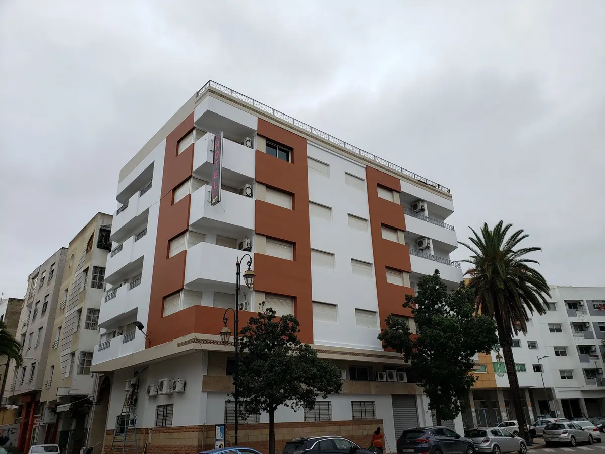 L'immeuble FIGUIG : façade blanche à bandes rouille, balcons superposés, palmiers sur le trottoir