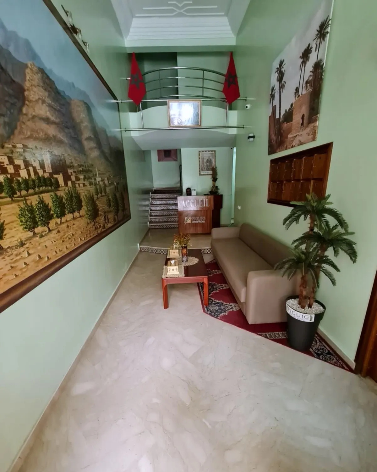 Hall d'entrée aux murs vert d'eau, grandes peintures d'oasis, comptoir « Accueil » et casier à clés au fond