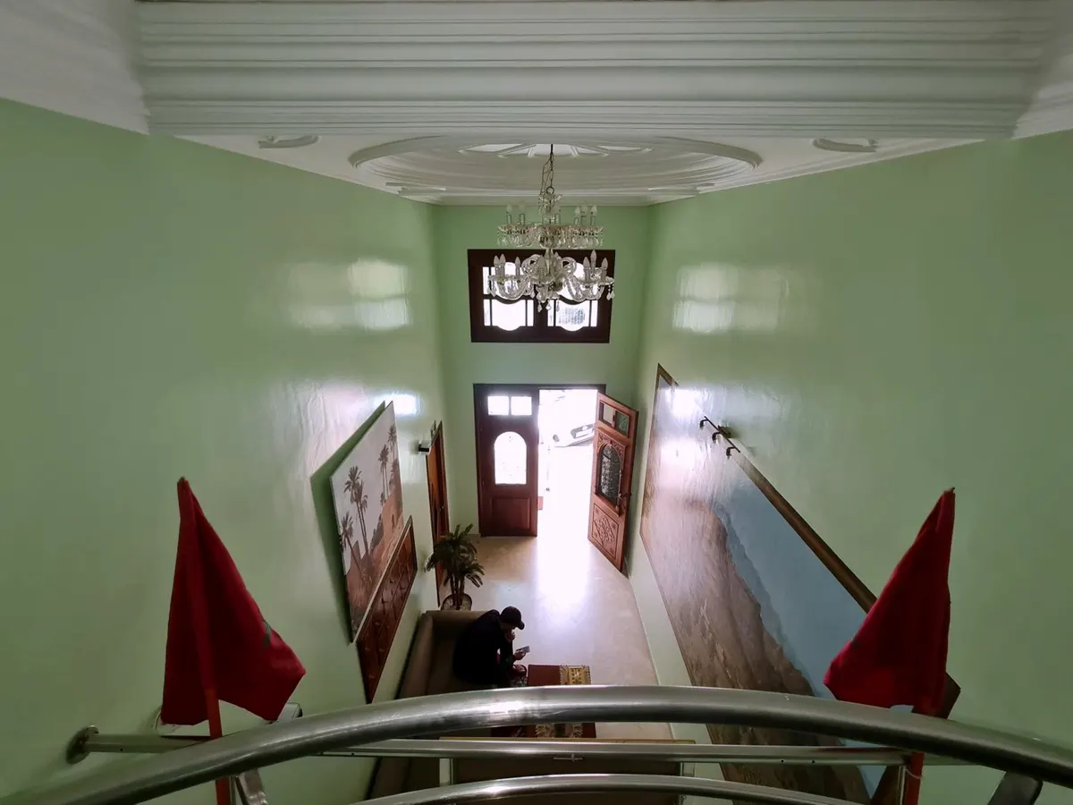 Le hall vu de la mezzanine : murs vert d'eau, lustre, drapeaux marocains, porte d'entrée