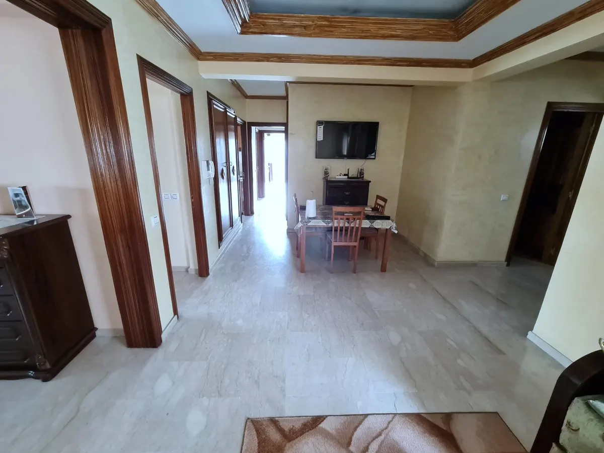 Entrée d'un appartement : couloir, plafond à caissons, coin repas et télévision au fond