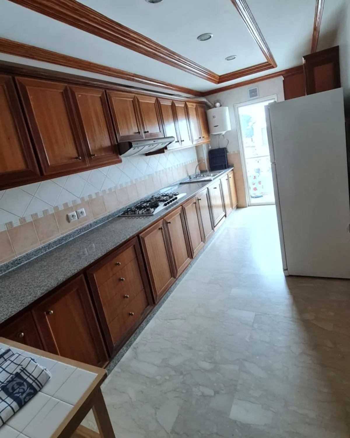 Cuisine en longueur avec placards en bois, plan de travail et réfrigérateur
