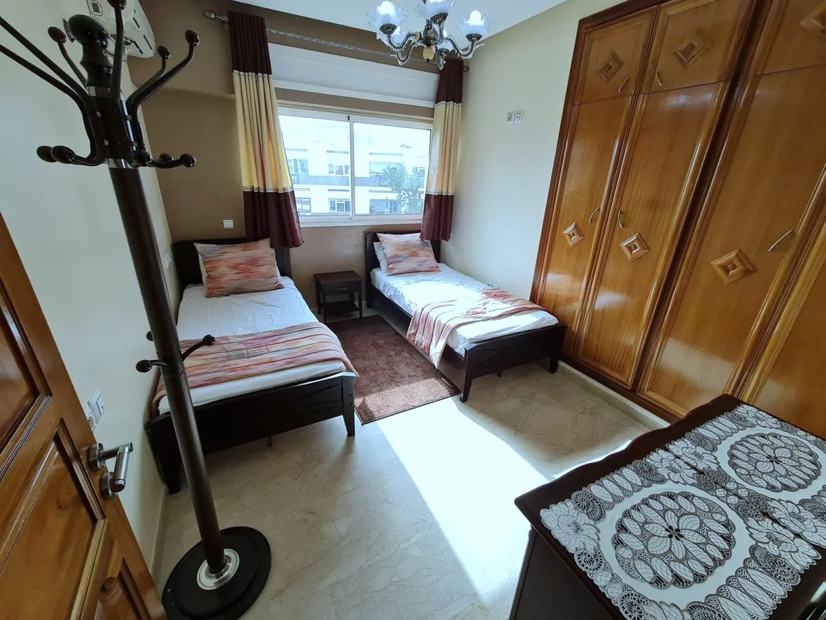 Chambre à deux lits simples, grande armoire en bois et portemanteau